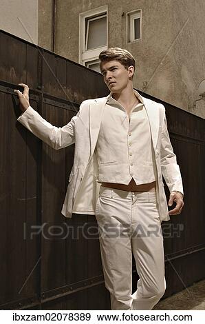 Stock Photo - Fashion photo of a young man wearing a white suit standing in front of a wooden fence. Fotosearch