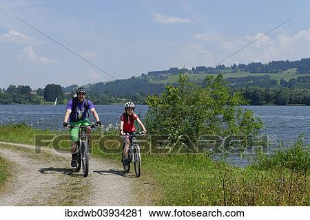 Stock Image - "Father and child on a bike tour at Rottachspeicher reservoir, Rottachsee Lake, Oberallgau, Swabia, Bavaria, Germany, Europe". Fotosearch