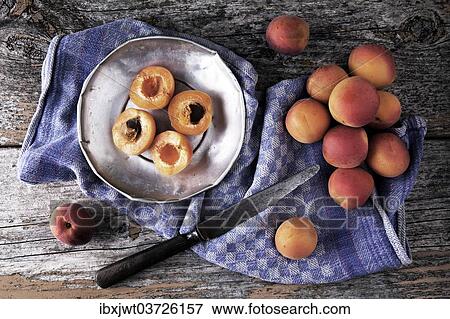 Stock Photo - "Fresh apricots on a tin plate, with a knife and kitchen towel on a wooden background". Fotosearch