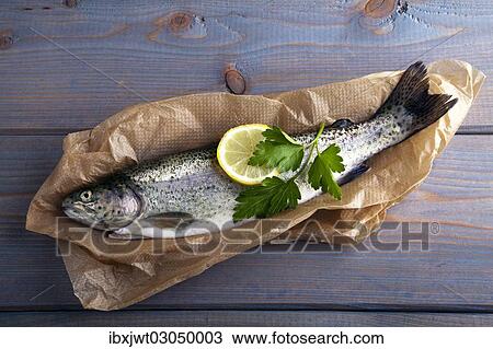 Stock Image - Fresh brook trout in baking paper on a wooden surface. Fotosearch