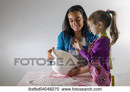 Stock Image - "Girl, 3 years, and her mother, baking, mixing ingredients in a white bowl". Fotosearch