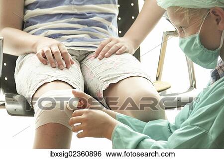 Stock Photograph - Girl and boy playing doctor with the boy dressed as a doctor wrapping a bandage around the girl's knee. Fotosearch