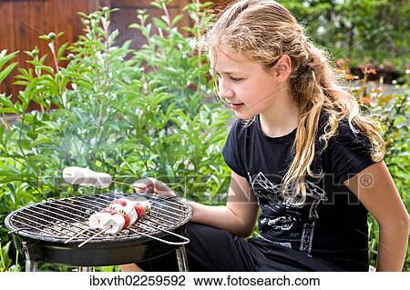 Stock Image - Girl barbecuing marshmallows in the garden. Fotosearch