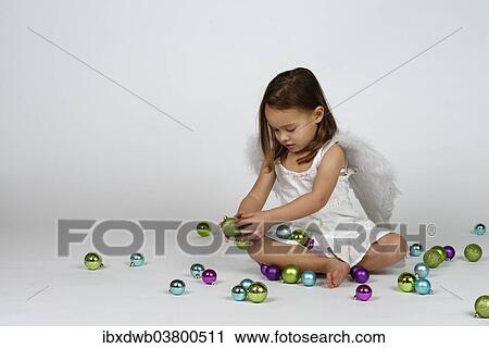 Stock Image - Girl dressed as an angel sits between Christmas baubles. Fotosearch
