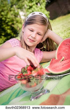 Stock Image - Girl eating strawberries in the garden. Fotosearch