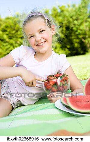 Stock Photograph - Girl eating strawberries in the garden. Fotosearch