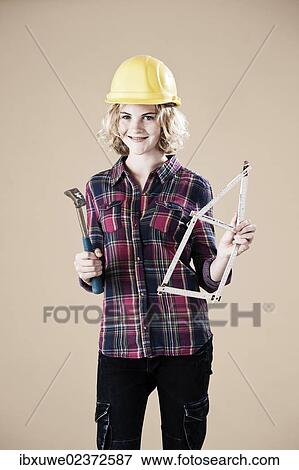 Stock Photo - Girl holding a hammer and a wooden ruler folded in the shape of a house. Fotosearch