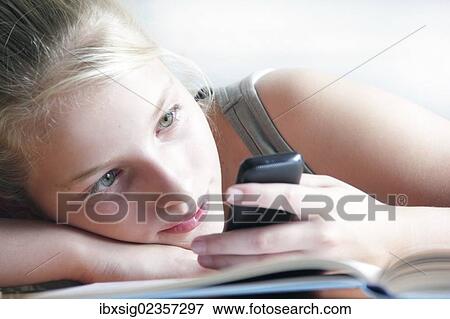 Stock Photo - Girl looking at a smartphone with her homework lying in front of her. Fotosearch