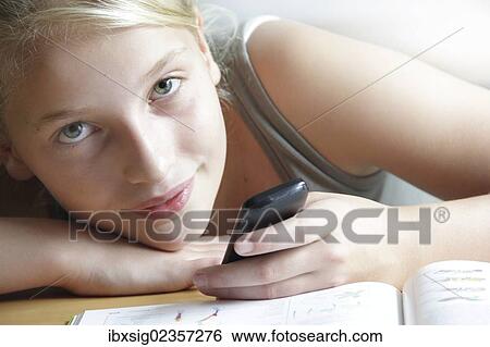 Girl looking at a smartphone with her homework lying in front of her View Large Photo Image Stock Photograph - Girl looking at a smartphone with her homework lying in front of her. Fotosearch