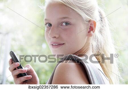 Stock Photograph - Girl looking towards the camera and holding a smartphone in her hand. Fotosearch