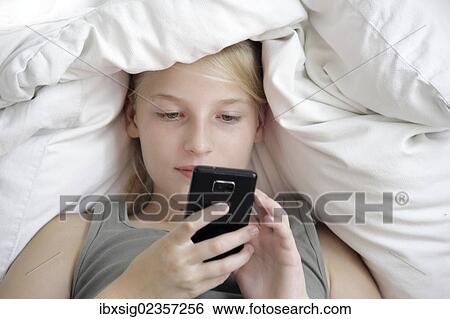 Girl lying in bed with a smartphone View Large Photo Image Stock Photograph - Girl lying in bed with a smartphone. Fotosearch