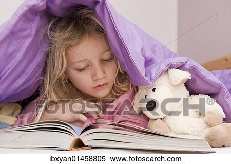 Stock Photography - Girl lying under bedspread reading a book. Fotosearch