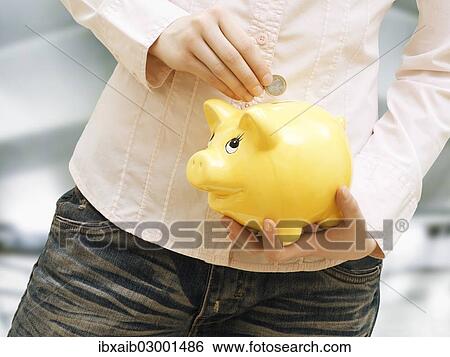 Stock Photograph - Girl putting euro coin into in piggy bank. Fotosearch