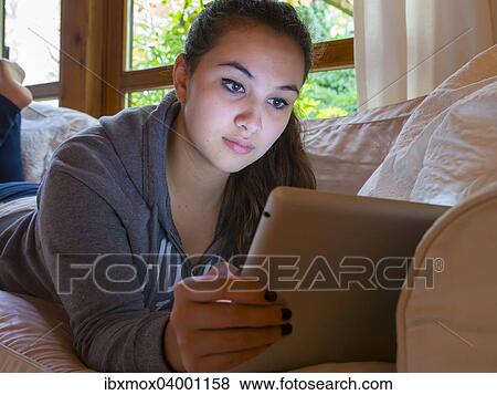 Stock Photo - "Girl reading on a tablet computer at home, Germany, Europe". Fotosearch