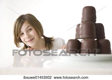 Stock Image - Girl sitting mischievously in front of a plate of chocolate marshmallows. Fotosearch