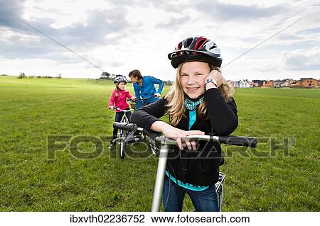 "Girl wearing a cycling helmet, her mother and sister at back, with bicycles, in front of rural landscape" View Large Photo Image Stock Image - "Girl wearing a cycling helmet, her mother and sister at back, with bicycles, in front of rural landscape". Fotosearch