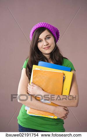 Picture - Girl with long hair wearing a hat and holding her school books in her arms. Fotosearch