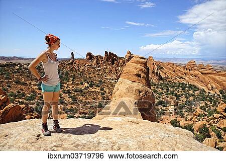Stock Photograph - "Hiker standing on Double O Arch with a view over Devil's Garden, with its sandstone formations created by erosion, Arches-Nationalpark, near Moab, Utah, United States, North America". Fotosearch