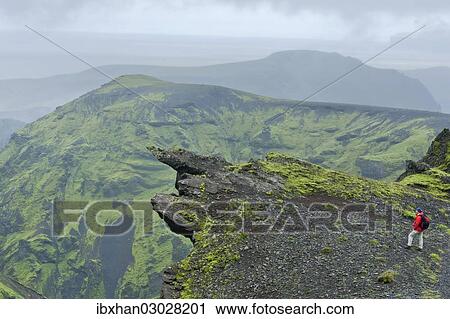 Stock Image - "Hiker standing on exposed rock along the trail from Pakgil canyon to Hoefoabrekkajoekull glacier, Pakgil, Iceland, Europe". Fotosearch