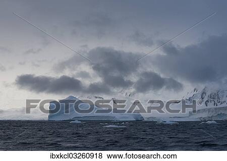 Stock Photo - "Iceberg in a fjord with mountain scenery and a cloudy sky, Gerlache Strait, Antarctic Peninsula, Antarctica". Fotosearch