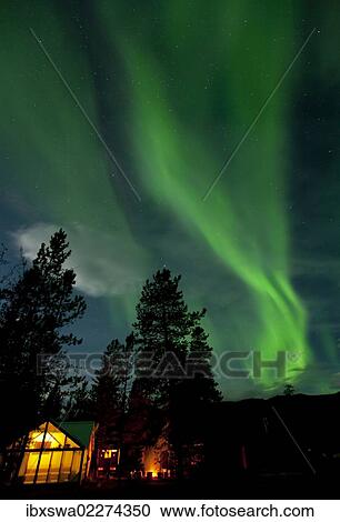 Stock Image - "Illuminated, lit wall tent, cabin with swirling northern polar lights, Aurora Borealis, green, near Whitehorse, Yukon Territory, Canada, North America". Fotosearch