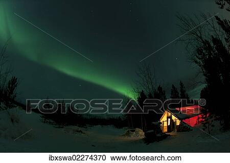 Stock Image - "Illuminated, lit wall tent, cabin with swirling northern polar lights, Aurora Borealis, green, near Whitehorse, Yukon Territory, Canada, North America". Fotosearch