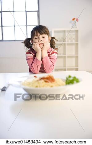 Little girl sitting listlessly in front of a plate of spaghetti View Large Photo Image Picture - Little girl sitting listlessly in front of a plate of spaghetti. Fotosearch