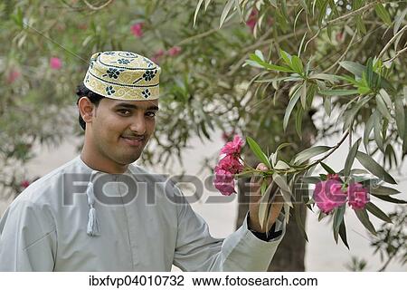 Stock Image - "Local man smelling a flower, Wadi Derbat, near Salalah, Dhofar Region, Orient, Oman, Asia". Fotosearch