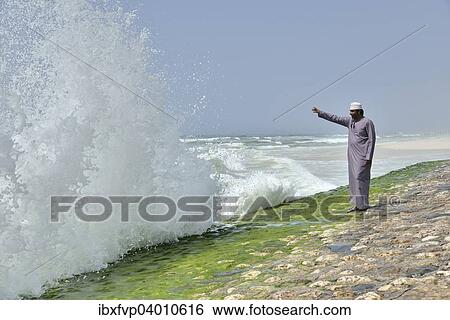 Stock Photograph - "Local man watching the surf at the corniche of Salalah during the monsoon season, or Khareef season, Salalah, Dhofar region, Orient, Oman, Asia". Fotosearch