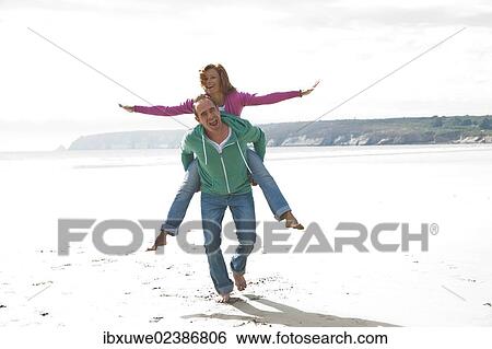 Man carrying a woman piggyback on a beach View Large Photo Image Stock Photograph - Man carrying a woman piggyback on a beach. Fotosearch