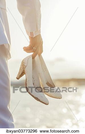 "Man holding white stiletto shoes, on a beach" View Large Photo Image Stock Photograph - "Man holding white stiletto shoes, on a beach". Fotosearch