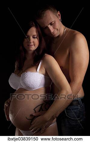 Stock Image - Man hugging his pregnant wife from behind. Fotosearch