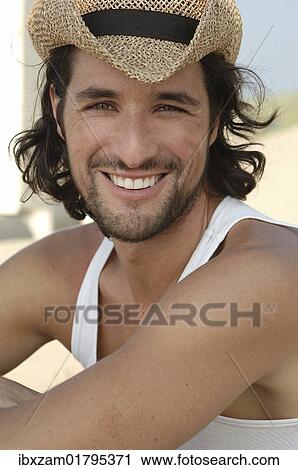 Stock Image - "Man wearing a sun hat on a beach, smiling". Fotosearch
