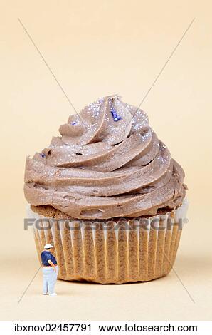 Stock Image - Miniature figurine standing in front of muffin. Fotosearch
