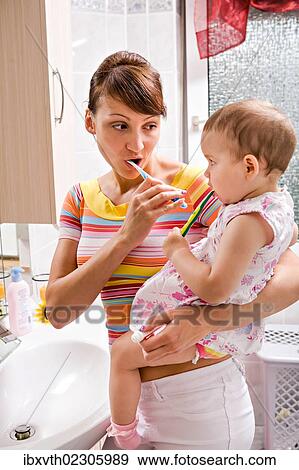 Stock Photo - "Mother and daughter brushing teeth together, bathroom". Fotosearch