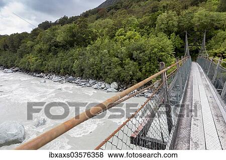Stock Photo - "Narrow suspension bridge over the Fox River, Fox River, West Coast Region, New Zealand, Oceania". Fotosearch