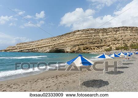 Stock Photo - "Neolithic cave dwellings in the yellow sandstone, parasols on the beach of Matala, former site of the hippies, Crete, Libyan Sea, Mediterranean, Greece, Europe". Fotosearch