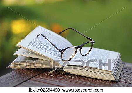 Stock Image - Old reading glasses with a book in the garden. Fotosearch