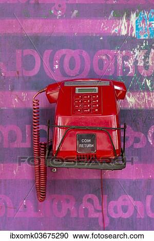 Stock Image - "Old red telephone against a wall with pink Malayalam script, Kerala, India, Asia". Fotosearch