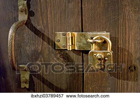Stock Photo - Old wooden door locked with metal fittings and a padlock. Fotosearch