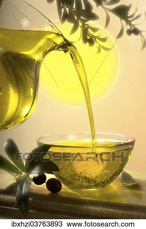 Stock Image - Olive oil being poured from a jug into a glass bowl. Fotosearch