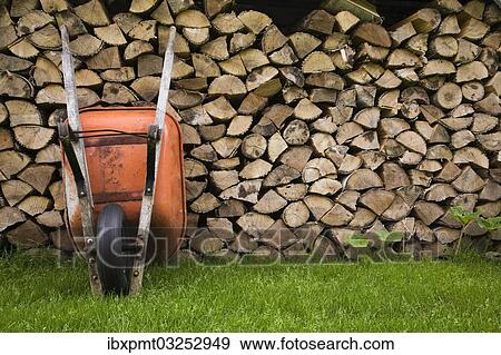 Stock Photo - "Orange wheelbarrow propped up against stacked firewood, Quebec City, Quebec Province, Canada, North America". Fotosearch