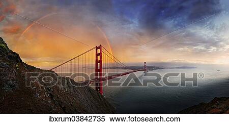 Stock Photography - "Panoramic view of the Golden Gate Bridge with a rainbow at sunset and orange-glowing storm clouds, San Francisco, California, United States, North America". Fotosearch