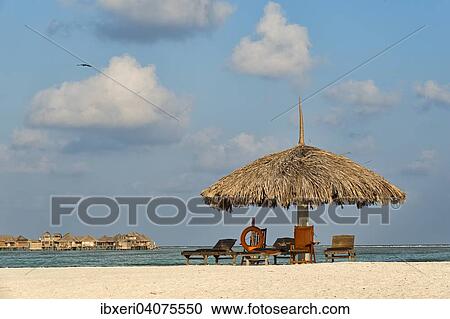 Stock Image - "Parasol, sunbeds and a lifebuoy on the beach, water bungalows at the back, Paradise Island, Maldives, Asia". Fotosearch