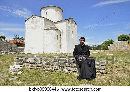 Stock Photography - "Pastor Zupnik don Bozo Baricic in front of the Church of the Holy Cross, Crkva svetoga Kriza, 9th century, the world's smallest cathedral, Nin, Zadar County, Dalmatia, Croatia, Europe". Fotosearch