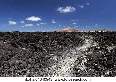 Stock Image - "Path through a lava field, volcanic landscape, Fire Mountains, volcanoes, Mancha Blanca volcano at the back, Lanzarote, Canary Islands, Spain, Europe". Fotosearch