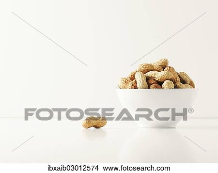 Picture - Peanuts in a white bowl with a single peanut beside it. Fotosearch