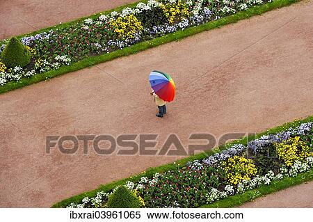 "Person with umbrella in rainbow colors on a red gravel path between flower beds in the castle gardens, Fuldaer Stadtschloss City Palace, Fulda, Hesse, Germany, Europe" View Large Photo Image Stock Photography - "Person with umbrella in rainbow colors on a red gravel path between flower beds in the castle gardens, Fuldaer Stadtschloss City Palace, Fulda, Hesse, Germany, Europe". Fotosearch