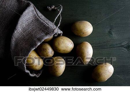 Stock Image - Potatoes in burlap sack on wood. Fotosearch