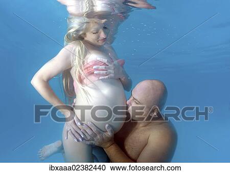 Stock Image - "Pregnant woman and man, underwater fashion in a pool". Fotosearch